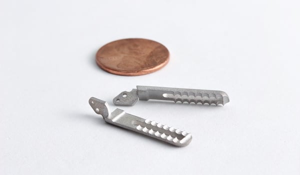 Prototypes for laparoscopic surgical grippers, printed in 17-4PH stainless steel with Holo's PureForm™ metal 3D printing technology, next to a penny that is roughly the same size as them.