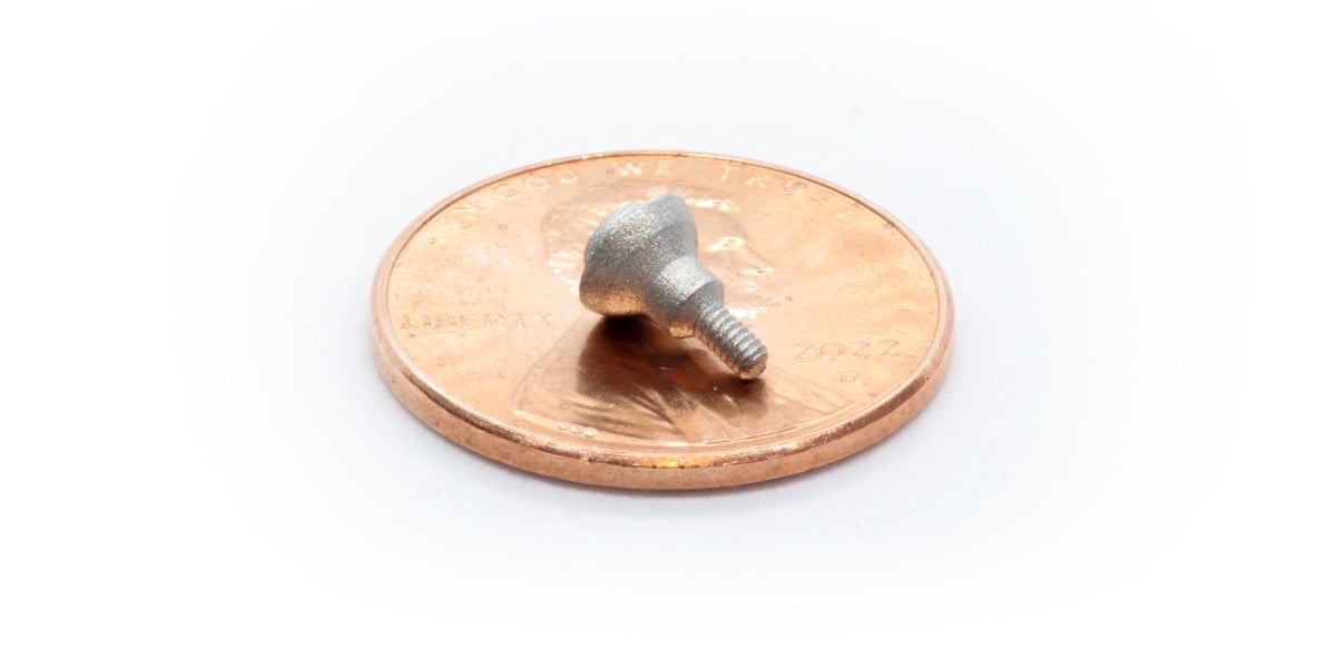 A custom medical screw sitting on top of a penny and occupying about 1/3 of the diameter of the penny face, built with Holo’s PureForm microAM process, demonstrating the tiny intricate features that can be printed directly into a larger part